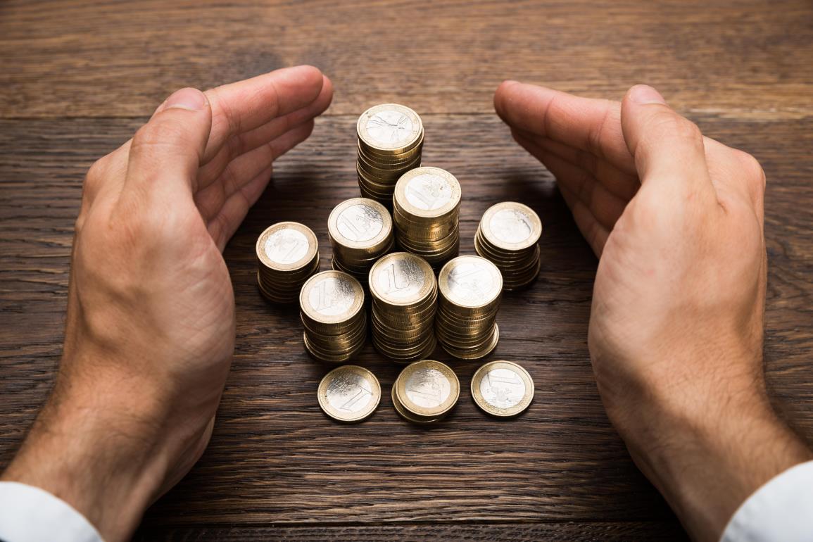 stock-photo-close-up-of-a-businessman-s-hand-protecting-stack-of-euro-coins-286869704